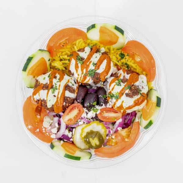 Mediterranean platter with falafel, yellow rice, creamy sauces, tomatoes, cucumbers, olives, pickles, red cabbage, and feta.