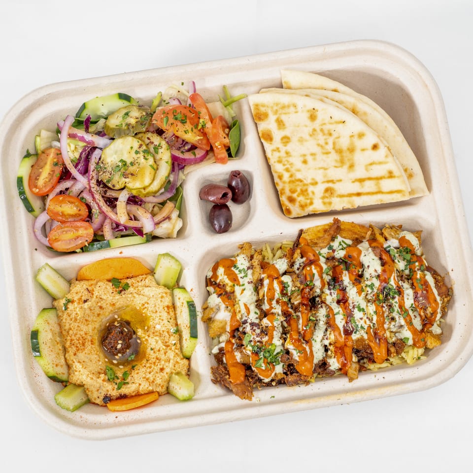 Mediterranean takeout platter with salad, grilled pita, hummus, olives, and saucy shawarma over rice.