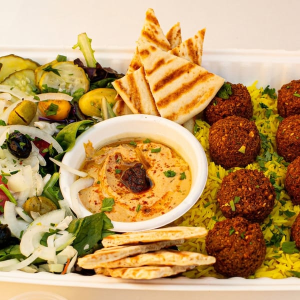 A falafel platter with hummus, pita bread, yellow rice, and a fresh salad in a white container.