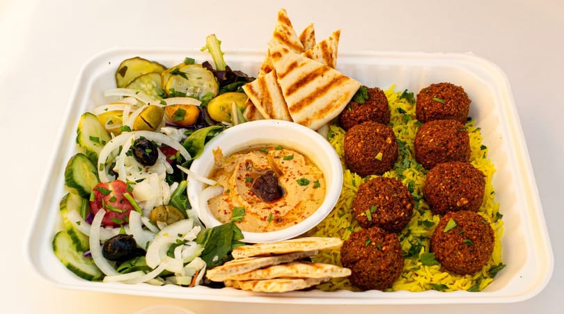 A falafel platter with hummus, pita bread, yellow rice, and a fresh salad in a white container.
