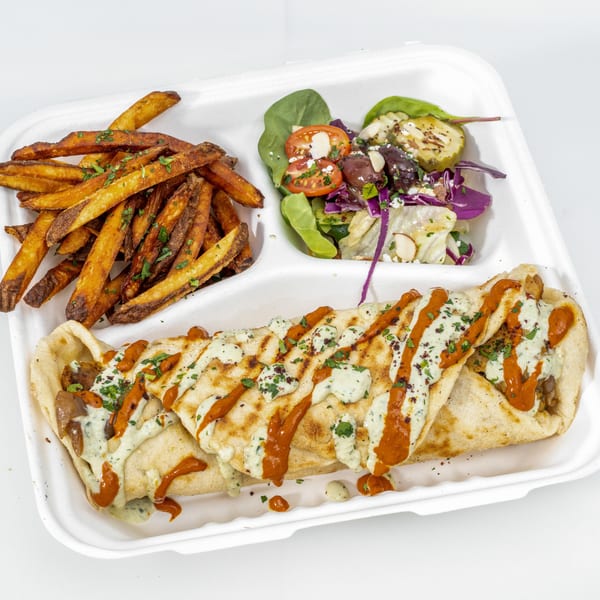 Takeout tray filled with sauced flatbread wraps, seasoned fries, and a colorful mixed salad.