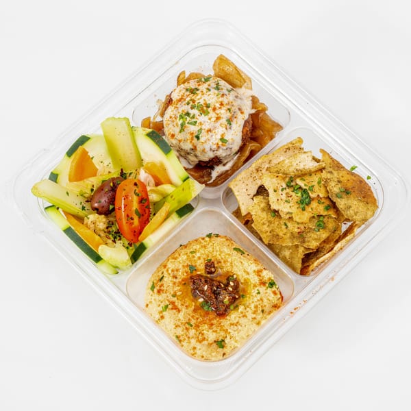 Mediterranean meal platter with hummus, grilled vegetables, salad, pita chips, and a creamy-topped meatball in a divided container.