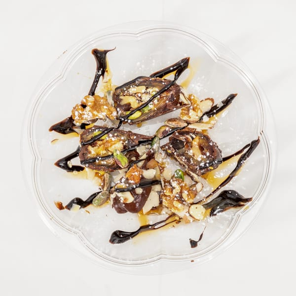 Dessert pieces topped with nuts, powdered sugar, caramel, and chocolate sauce on a clear serving plate.