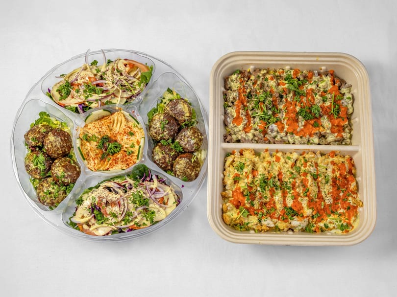 A platter of falafel, hummus, and salads next to a container of two rice dishes.
