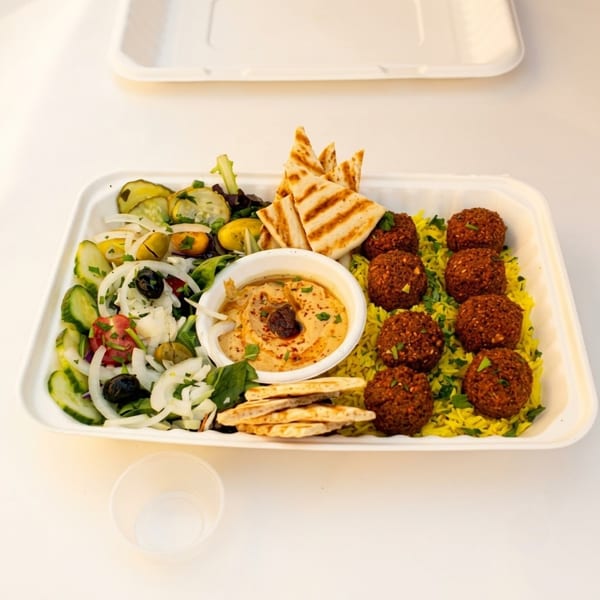 Falafel plate with yellow rice, hummus, salad, and pita bread in a takeout container.