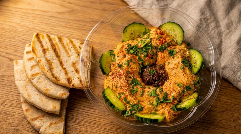 Hummus with cucumber slices, parsley, and a dark topping, served with grilled pita bread.