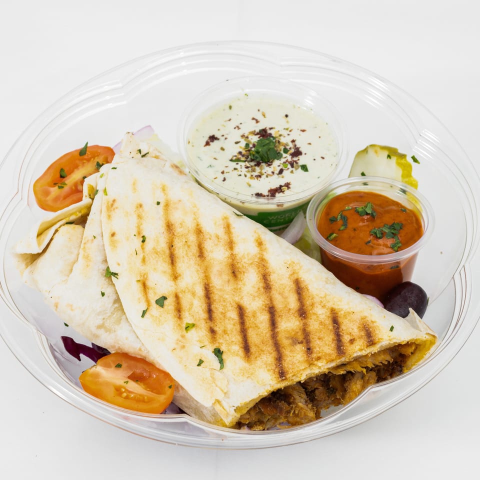 Grilled stuffed flatbread served with creamy herb sauce, red dipping sauce, tomatoes, lettuce, cucumber, and olives.