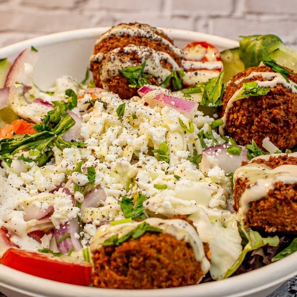 Falafel salad bowl with crumbled feta, red onions, cucumbers, tomatoes, and a creamy dressing.