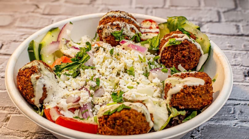 Falafel salad bowl with crumbled feta, red onions, cucumbers, tomatoes, and a creamy dressing.
