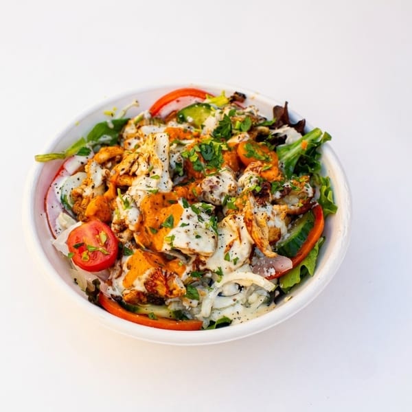 Vibrant salad with greens, tomatoes, cucumbers, chicken, creamy white and orange sauces in a white bowl.